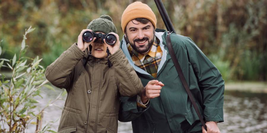 Kind mit Fernglas und Jäger vor einem See (Symbolbild: iStock/LightFieldStudios)