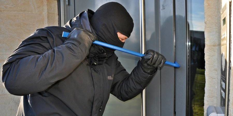 Ein maskierter Mann versucht mit einem Brecheisen eine Wohnungstüre aufzuhebeln. (Symbolbild: Steffen Salow)