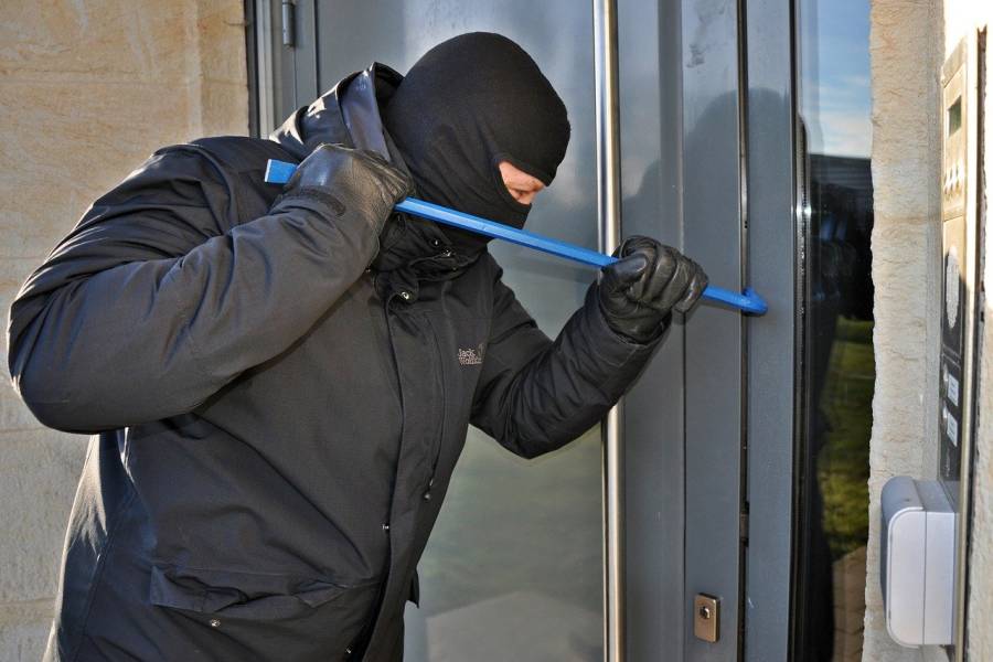 Ein maskierter Mann versucht mit einem Brecheisen eine Wohnungstüre aufzuhebeln. (Symbolbild: Steffen Salow)