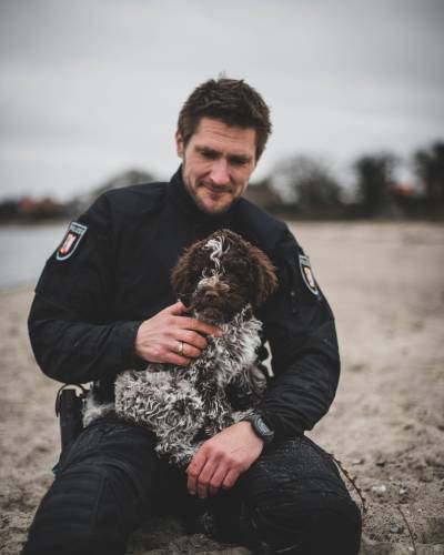 „Sky“ ist eine 12 Wochen alte Hündin der Rasse Lagotto Romagnolo. Hier zu sehen mit ihrem Hundeführer. (Foto: POL-SH-AFB)