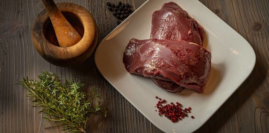 Wildbret vom Hirsch mit rosa Beeren, Wacholder und Rosmarin neben einem Mörser (Symbolbild: wax111)