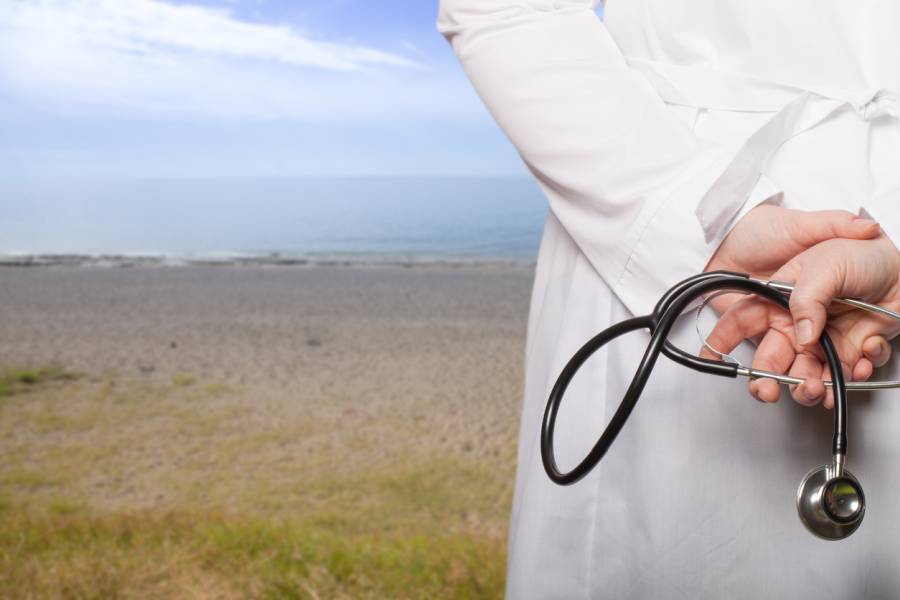 Ein Arzt, der in seinen Händen auf dem Rücken ein Stethoskop hält, blickt aufs Wasser. (Symbolbild: iStock/Strannik_fox)
