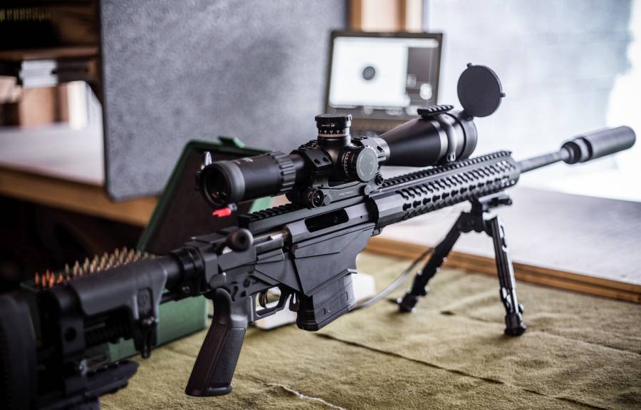 Modernes Repetiergewehr mit Zielfernrohr und Schalldämpfer auf einem Schießstand. Im Hintergrund eine Box mit Munition und ein Monitor zur Trefferaufnahme. (Symbolbild: iStock/IndiaUniform)