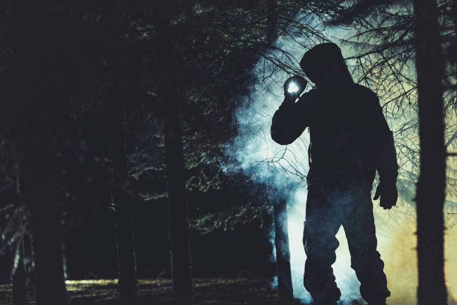 Ein dunkel gekleideter und vermummter Mann mit Taschenlampe nachts im Wald. (Symbolbild: iStock/welcomia)