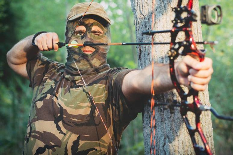 Ein maskierter Mann in Tarnkleidung mit Pfeil und Bogen. (Symbolbild: iStock/zorandimzr)