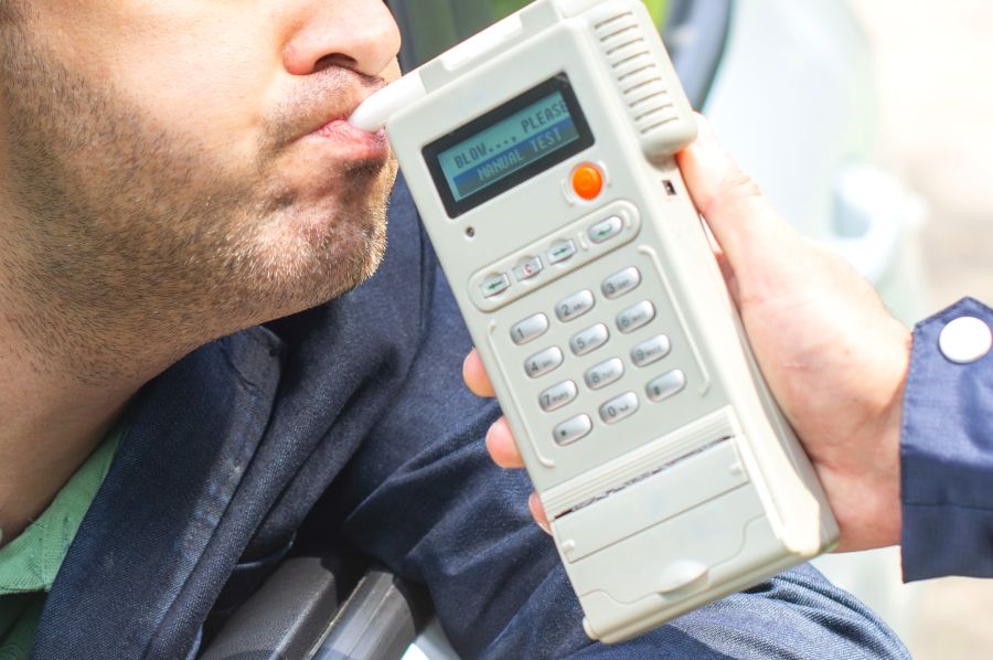 Ein Mann bläst in ein Testgerät während einer Atemalkoholkontrolle der Polizei. (Symbolbild. iStock/Tutye)