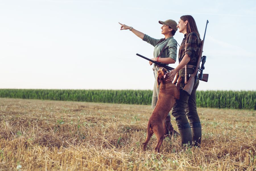 Zwei Jägerinnen mit einem Jagdhund auf einem abgeernteten Feld. (Symbolbild: iStock/zorandimzr)