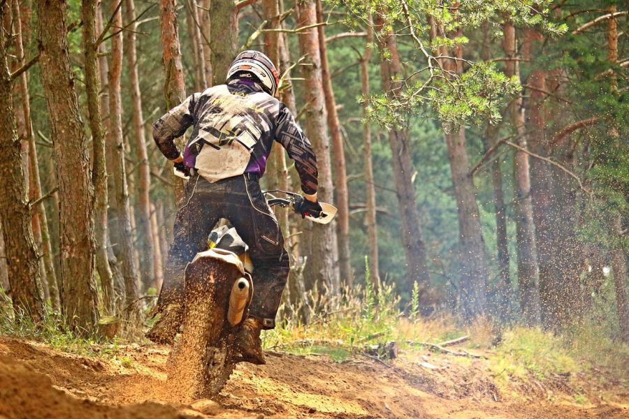 Ein Motocross-Fahrer, der mit seiner Maschine durch den Wald fährt. (Symbolbild: rihaij auf Pixabay)