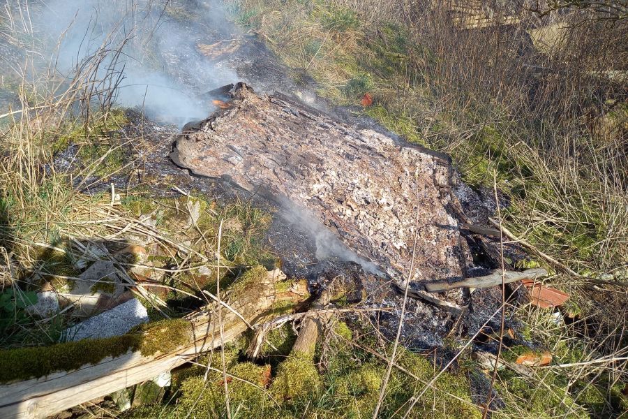 Teile der Teerpappe, die wahrscheinlich einmal das Hochsitzdach abgedichtet hatte, sind auf dem verkohlten Rasen noch zu erkennen. (Foto: Polizei NB)